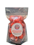 A clear plastic zip-top bag containing bright red freeze-dried marshmallows, with a round white label reading 'Freeze-Dried Marshmallows' and a cartoon mascot logo, placed on a dark surface.